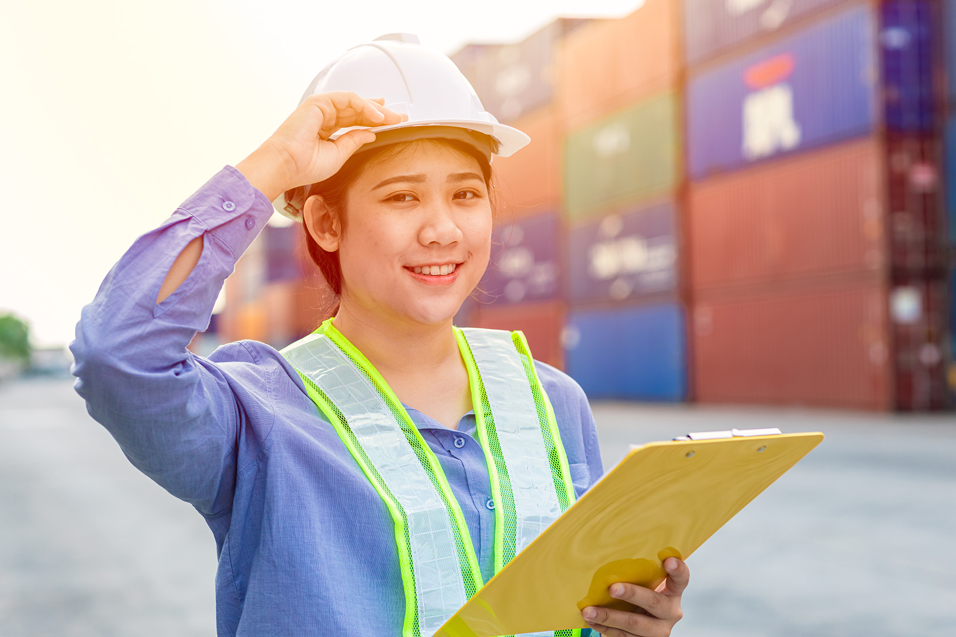 Portrait of Asian girl teen worker working in shipping cargo port import export working area with container box background.